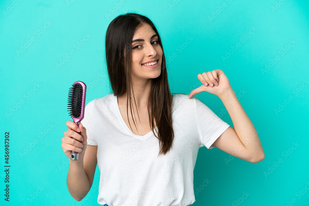 Young caucasian woman with hair comb isolated on blue background proud and self-satisfied Young caucasian woman with hair comb isolated on blue background proud and self-satisfied