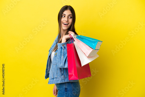 Young caucasian woman isolated on blue background holding shopping bags and looking back