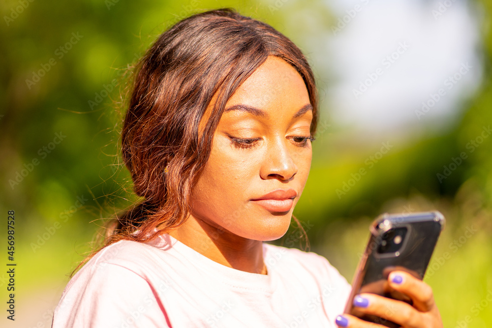 Young black woman with her phone chatting with her friends in a park on an October afternoon. Young black woman with her phone chatting with her friends in a park on an October afternoon.