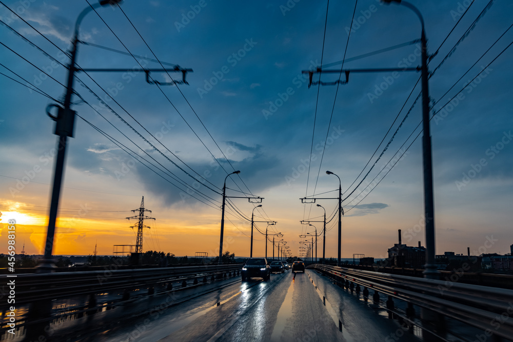 City bridge with wires for trolleybus in the rain at sunset.