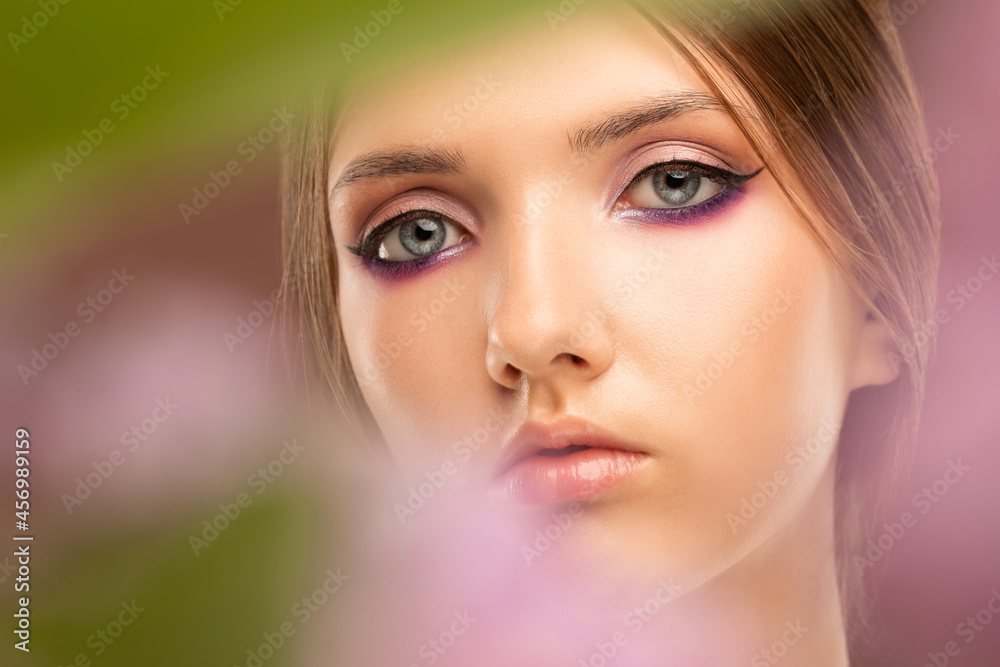 Portrait of attractive girl with healthy clean skin and beautiful make-up against the background of lilac flowers. Aesthetic cosmetology and makeup concept.