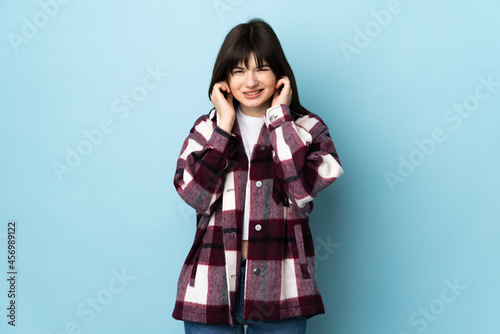 Teenager Ukrainian girl isolated on blue background frustrated and covering ears © luismolinero