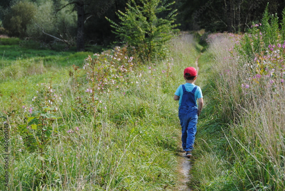 ein kind in rote mütze und jeans overall rennt auf natur weg ein kind in rote mütze und jeans overall rennt auf natur weg