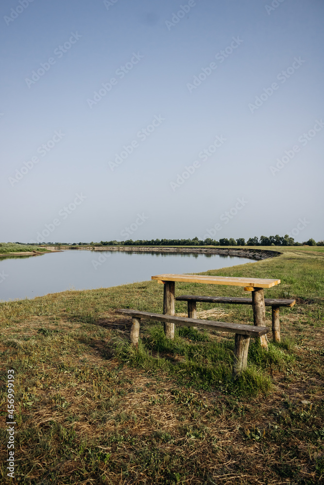 Beautiful summer landscape by the river. Wooden table and benches by the river. Pripyat river, Belarus Beautiful summer landscape by the river. Wooden table and benches by the river. Pripyat river, Belarus