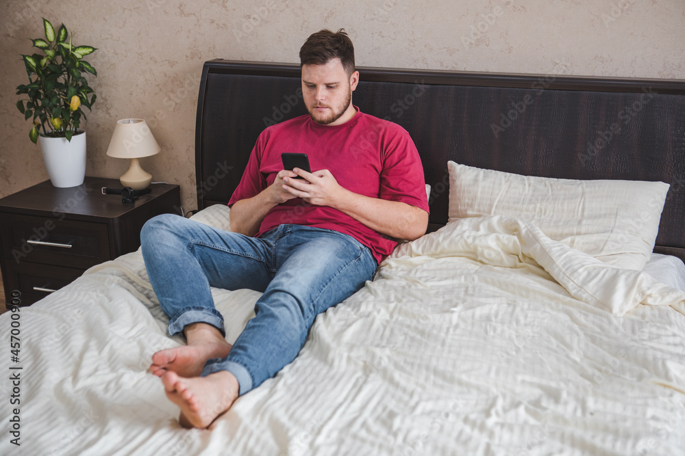 man sitting in bed surfing internet on the phone