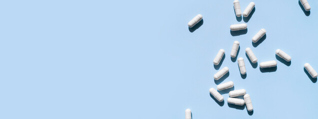 Pills, tablets, vitamins, food supplement in white capsules with shade from sun on blue background. Health concept vitamin deficiency avitaminosis medical pharmaceutical background Flat lay top view
