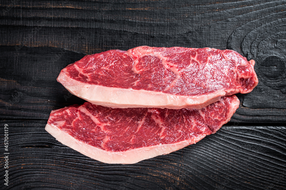 Raw rump steak or top sirloin cap beef meat steaks on butcher table. Black wooden background. Top view