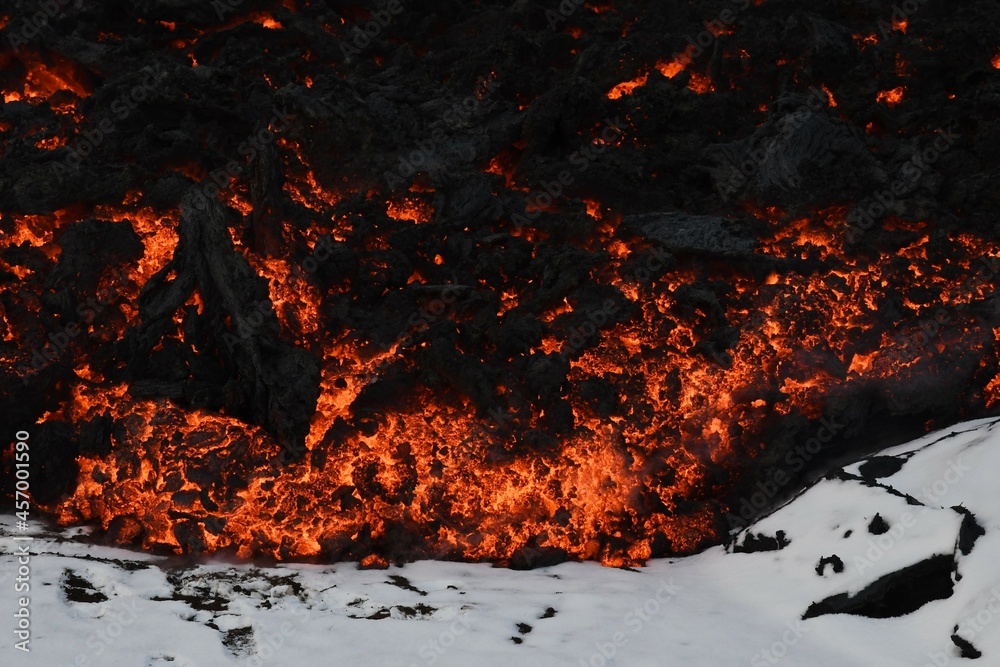 Lava flow at Fagradalsfjall, Iceland. Molten red and orange lava flows over white, snowy ground. The cooled lava forms a black crust. Lava flow at Fagradalsfjall, Iceland. Molten red and orange lava flows over white, snowy ground. The cooled lava forms a black crust.