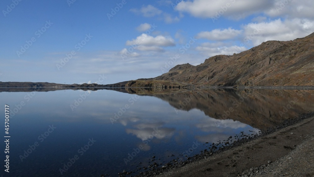 Lake Kleifarvatn in Iceland. Perfectly calm water with reflection of the mountains and sky. Blue sky in the background with white clouds.