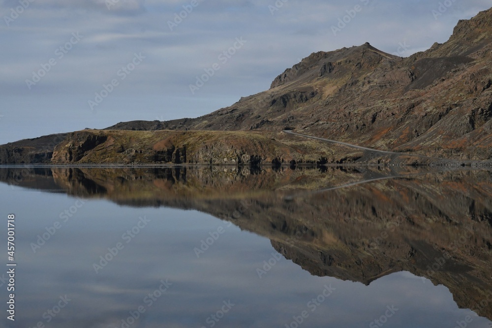 Lake Kleifarvatn in Iceland. Perfectly calm water with reflection of the sky and mountains. The mountains are brown and green. 