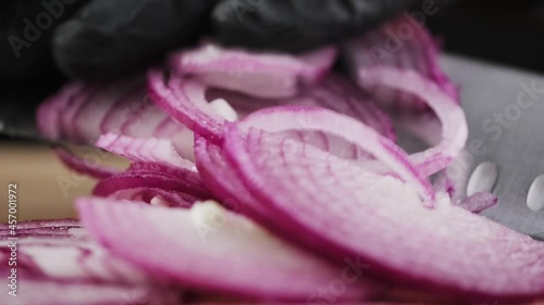 Close-up of a chef's hand cuts a red onion with a knife on a wooden board. Cutting onions with a knife. 