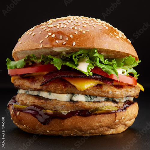 Yummy grilled chicken burger with double cutlet and cheese on a black background. Side view, close-up