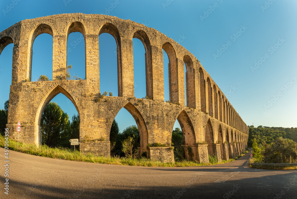 Panoramic view of the Pegões Aqueduct, near the city of Tomar in Portugal, lit by the sun at the end of the day with a blue sky in the background.