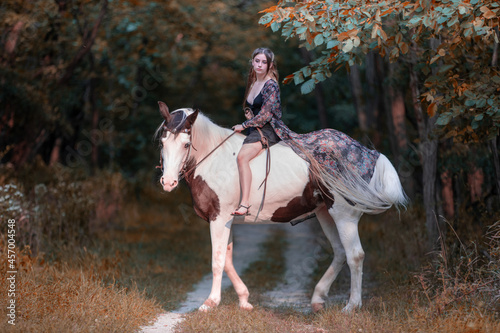 Image of a girl riding a horse in a forest during fall at sunset