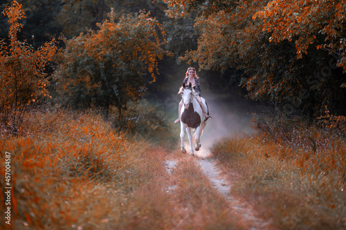 Image of a girl riding a horse in a forest during fall at sunset