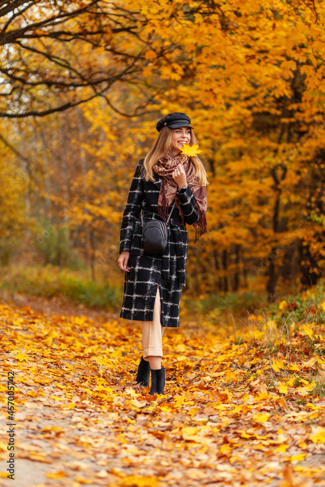 Pretty young smiling woman in fashion clothes with yellow leaf walking in the park with colorful golden foliage Pretty young smiling woman in fashion clothes with yellow leaf walking in the park with colorful golden foliage
