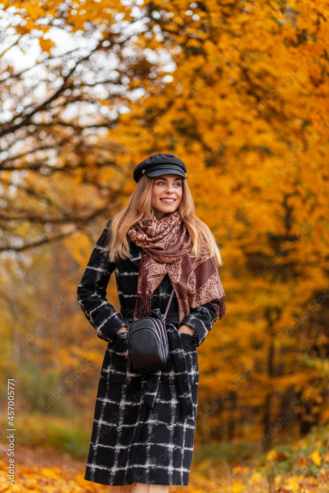 Happy beautiful young smiling woman with a scarf and a hat in a fashionable coat walks in an autumn forest with amazing yellow foliage Happy beautiful young smiling woman with a scarf and a hat in a fashionable coat walks in an autumn forest with amazing yellow foliage