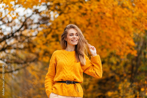 Happy pretty scandinavian woman with a beautiful smile in a fashionable yellow knitted sweater walks in an autumn park with colored fall foliage
