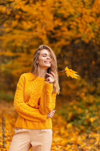 Happy young woman with cute smile in fashion vintage knitted yellow sweater with golden leaf in nature with amazing colored leaves