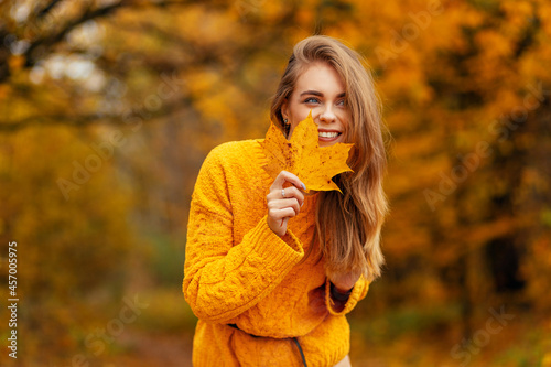 Funny pretty young smiling girl in fashion knitted yellow sweater with colored fall leaf enjoy a autumn day outdoors