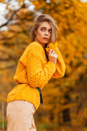 Autumn portrait of a beautiful young woman in a vintage knitted sweater with an autumn yellow leaf in nature with bright golden foliage