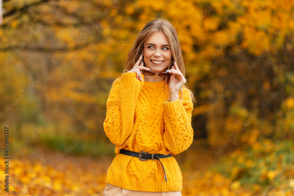 Portrait of a beautiful young girl with a sweat smile in a fashionable knitted yellow sweater wears sunglasses outdoors with bright golden fall foliage Portrait of a beautiful young girl with a sweat smile in a fashionable knitted yellow sweater wears sunglasses outdoors with bright golden fall foliage