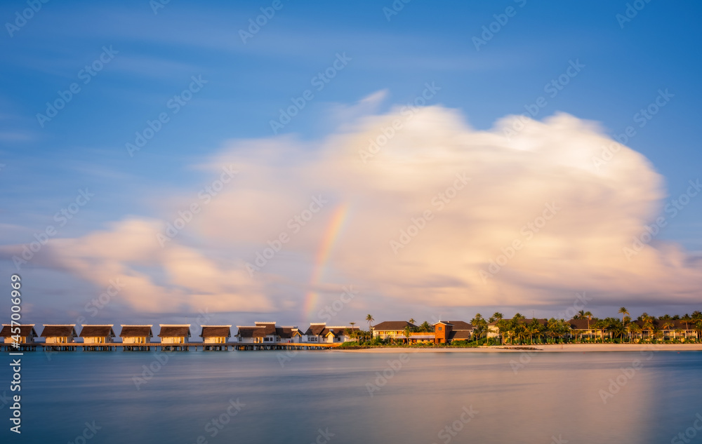 Obraz premium Island in ocean, overwater villas at the time sunset with rainbow. Crossroads Maldives, saii lagoon hotel. July 2021. Long exposure picture