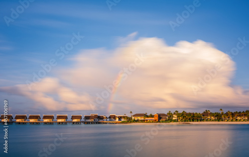 Island in ocean, overwater villas at the time sunset with rainbow. Crossroads Maldives, saii lagoon hotel. July 2021. Long exposure picture