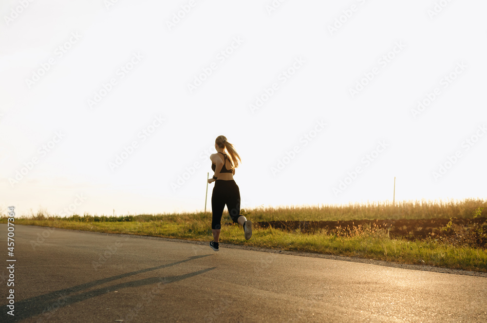 Fototapeta premium Young sporty girl running on a road at sunset. Lifestyle sports motivation. 