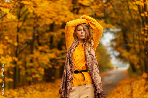 Pretty European woman in vintage knitted yellow sweater and fashion scarf poses in the amazing park with colorful autumn leaves. Female fall style and beauty
