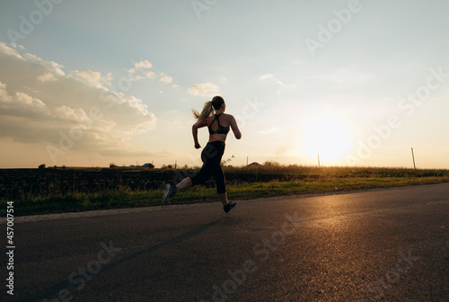 Young sporty girl running on a road at sunset. Lifestyle sports motivation. 