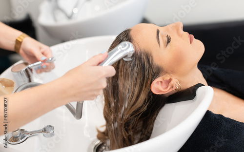 Hair stylist at work - hairdresser washing blond hair to the woman customer with eyes closed