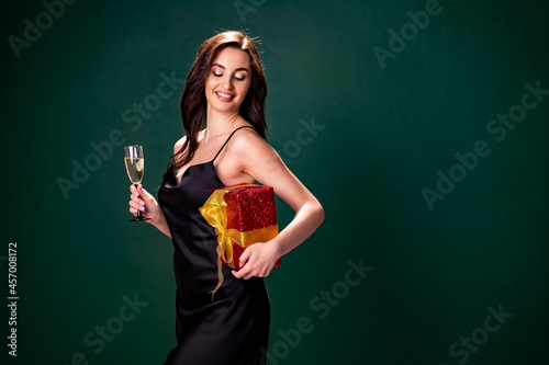 woman in black dress holds the gift red box and glass of champagne. Party time. Holiday concept