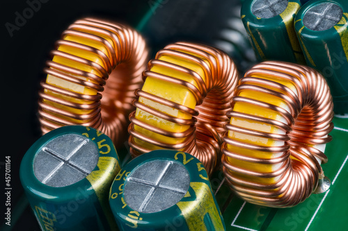 Yellow ferrite cores of toroidal inductors wrapped with copper wire on green printed circuit board. Closeup of electronic components. Coils or electrolytic capacitors on PCB detail of DC-DC converter.