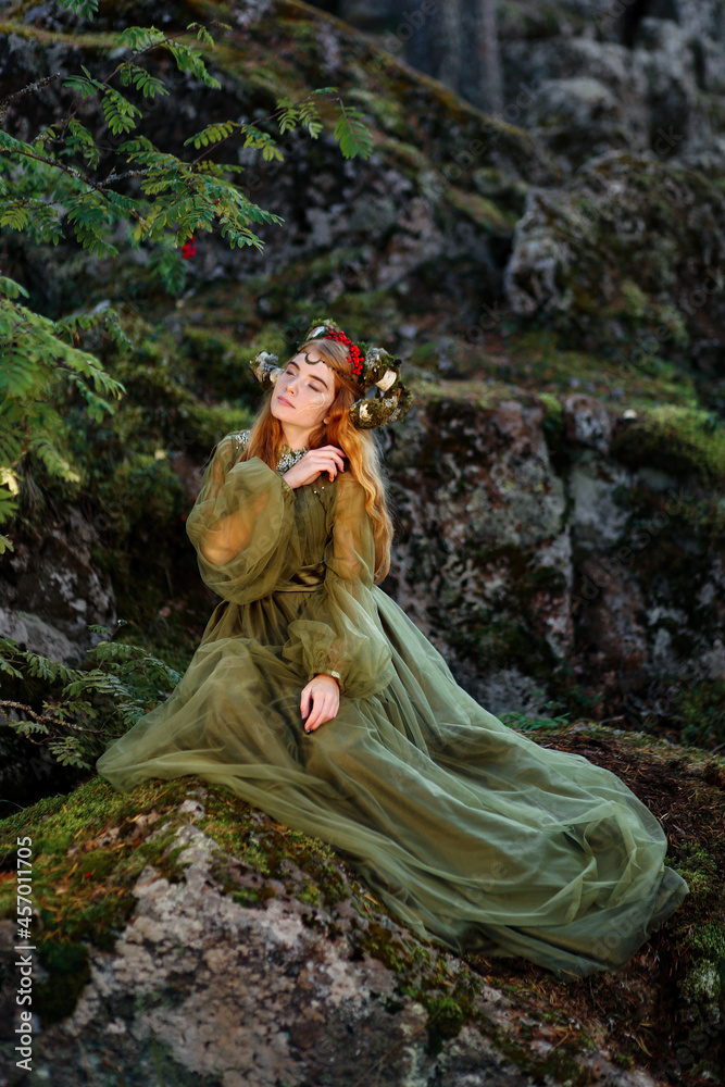 Beautiful red haired girl with mossy horns wearing green dress and sitting on mossy rocks Beautiful red haired girl with mossy horns wearing green dress and sitting on mossy rocks