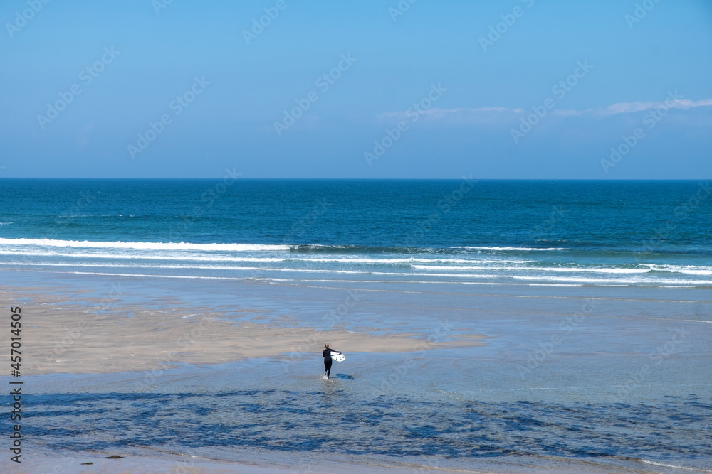 An unrecognizable woman walks towards the sea to surf at Praia de Moledo beach. Caminha municipality. Portugal.