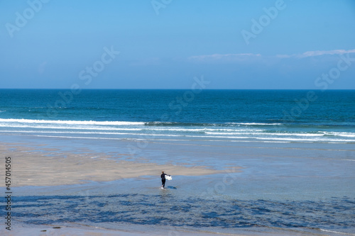 An unrecognizable woman walks towards the sea to surf at Praia de Moledo beach. Caminha municipality. Portugal.