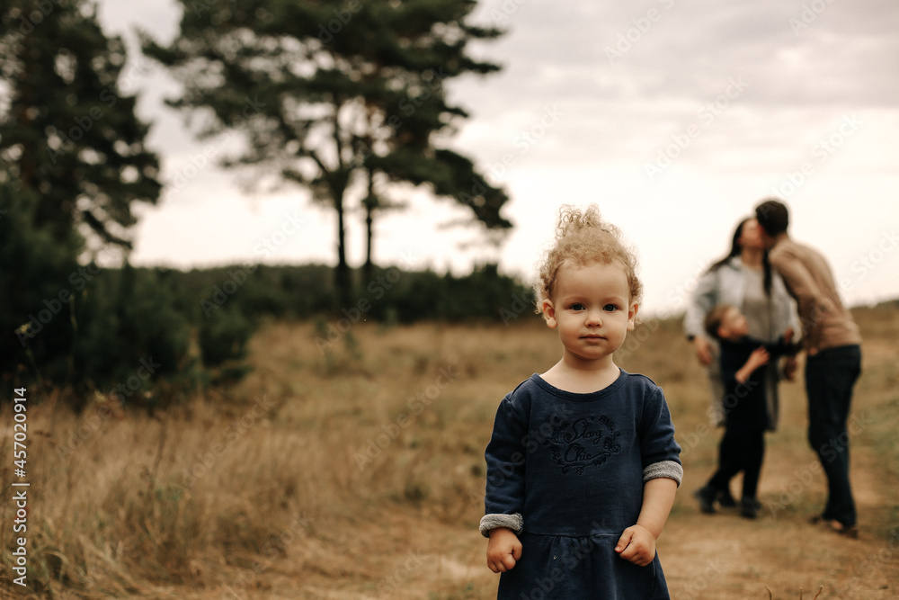 Little curly girl stands in the forest and her parents hugging in the background Little curly girl stands in the forest and her parents hugging in the background