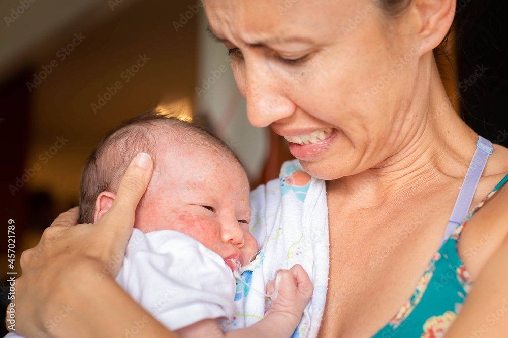 A worried mother holding her sick newborn baby at home. Infant