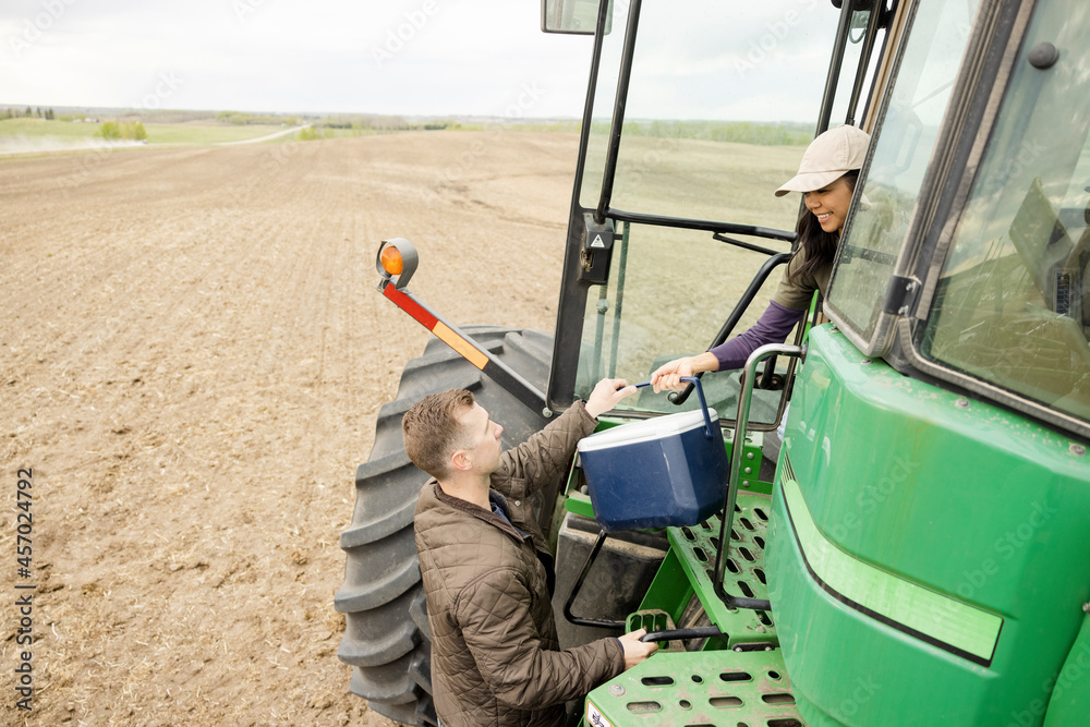 Farmer husband handing cooler to wife driving tractor on farm Stock ...