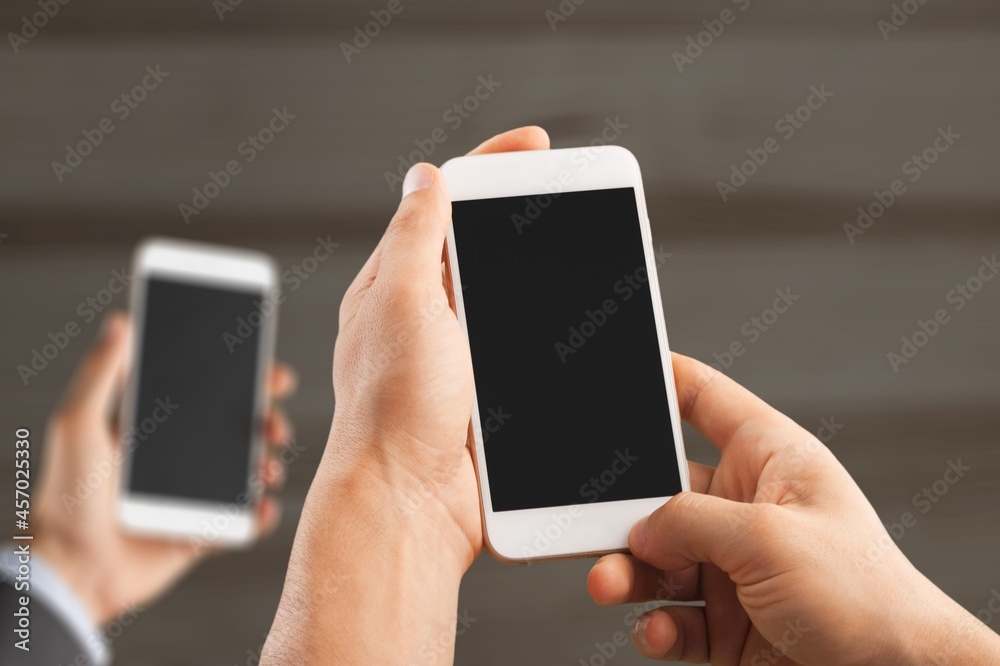 Two modern smartphones with blank screens in human hands