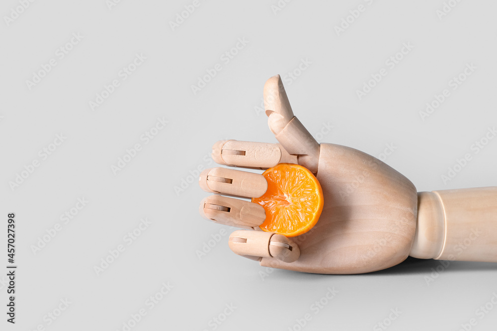 Obraz premium Wooden hand with cut mandarin showing thumb-up on light background