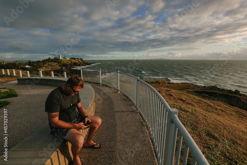 Digital nomad man working on phone during early morning walk at the Lambert's Beach lookout in Mackay, Queensland Australia