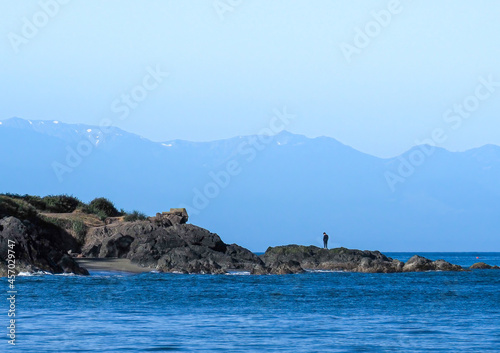 Lone person standing on rocky shore overlooking Rosario Strait in the San Juan Islands with the Cascade Mountains in the distance. © Dawn