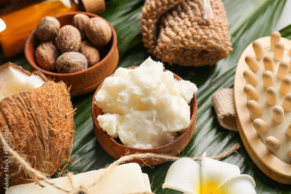 Bowl of shea butter, nuts and bath supplies on green leaves, closeup