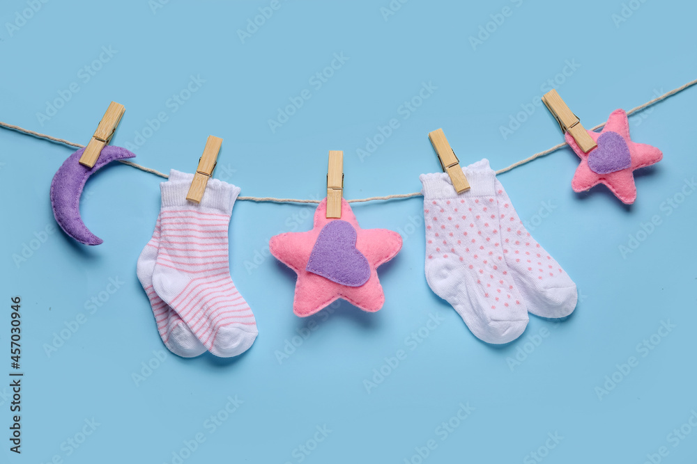Baby socks and toys hanging on rope against color background Baby socks and toys hanging on rope against color background