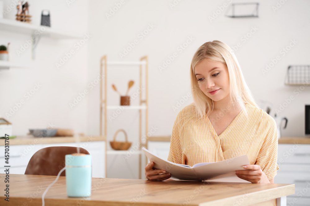 Woman with modern humidifier sitting at table in kitchen Woman with modern humidifier sitting at table in kitchen