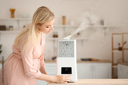 Pregnant woman with modern humidifier in kitchen photo