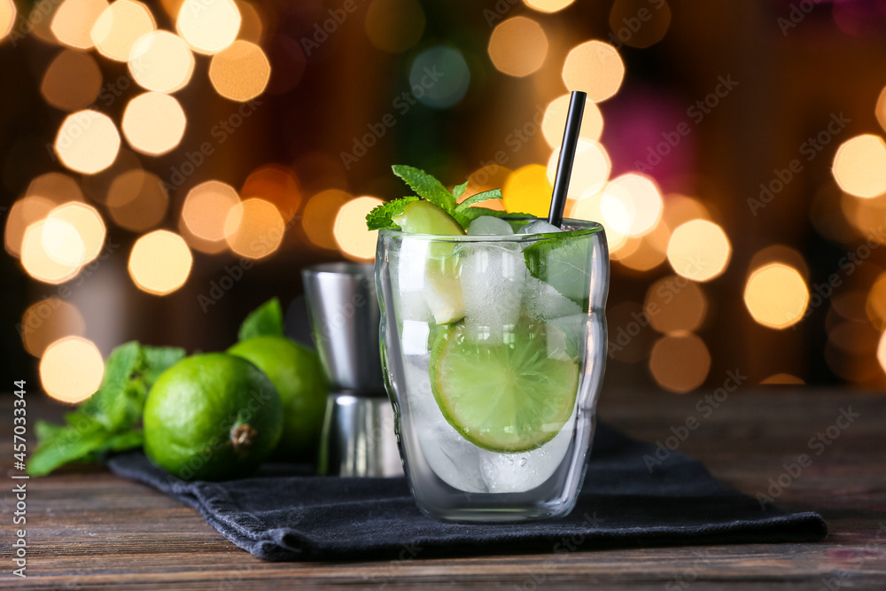 Glass of cold mojito on table against blurred lights