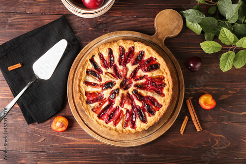Board with tasty plum pie on wooden background